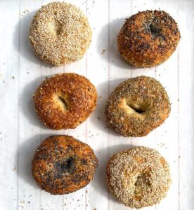 6 assorted bagels on a white wooden tray, sesame, poppy, parmesan garlic, sesame