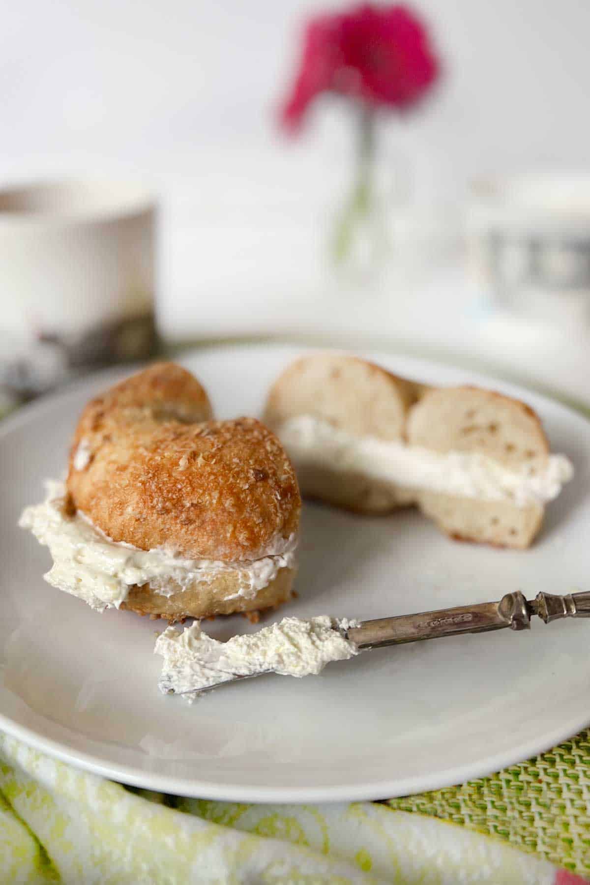 sliced parmesan garlic bagel with cream cheese on a white plate with a pink flower in the background