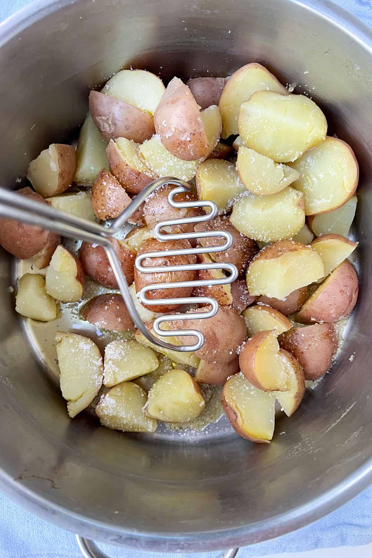 potato masher about to mash boiled red skin potatoes that are in a silver cooking pot