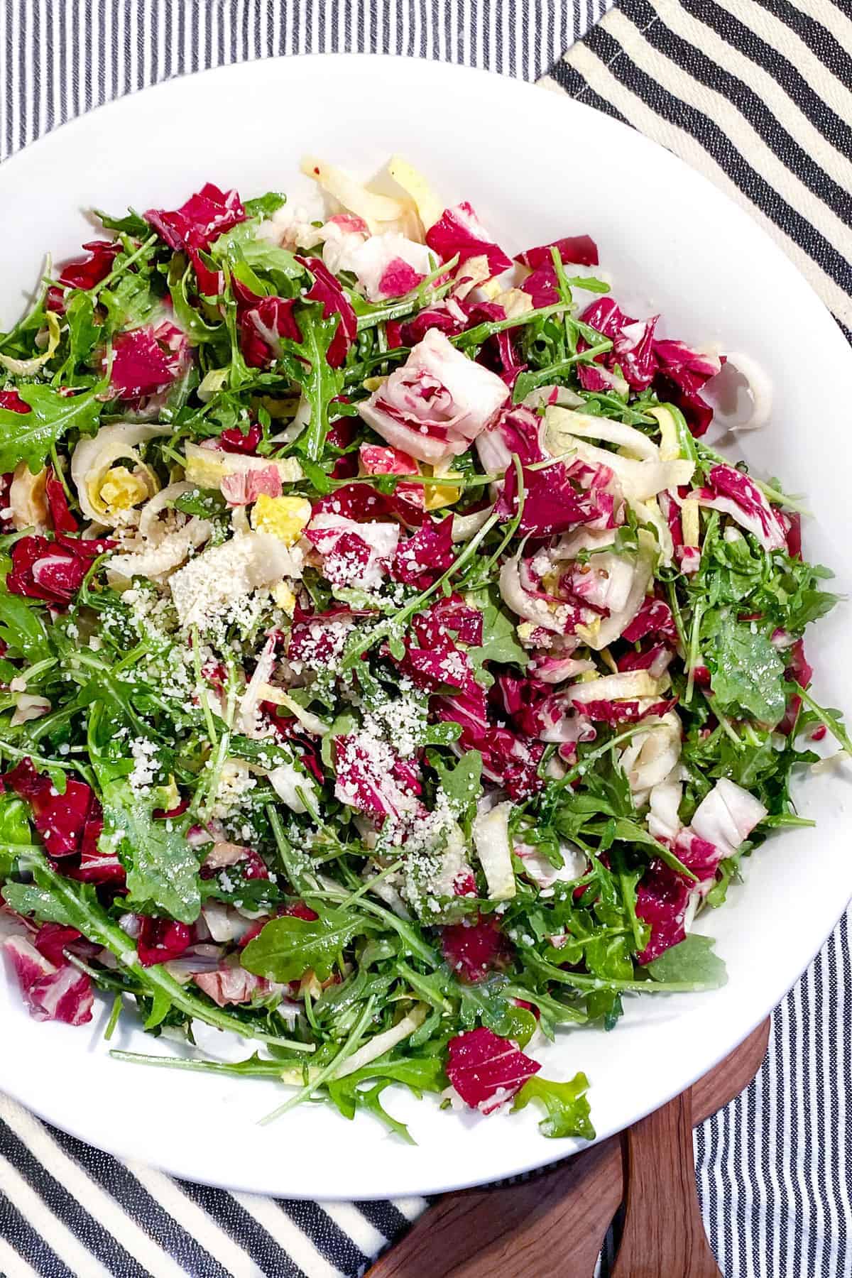 White serving bowl filled with colorful chopped lettuces, arugula, radicchio and endive, sprinkled with parmesan cheese.