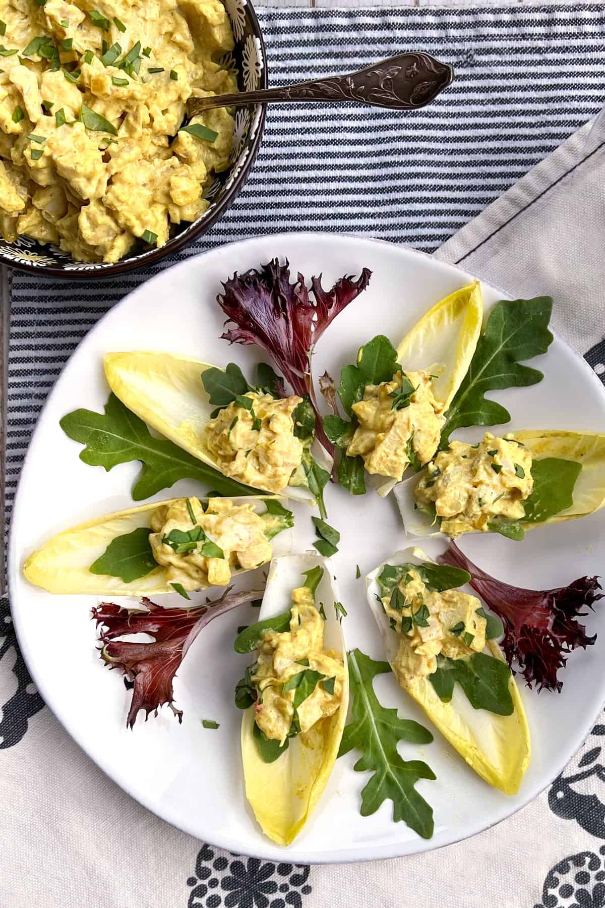 6 Endive spears on a round white platter, each topped with curried chicken salad and an endive leaf
