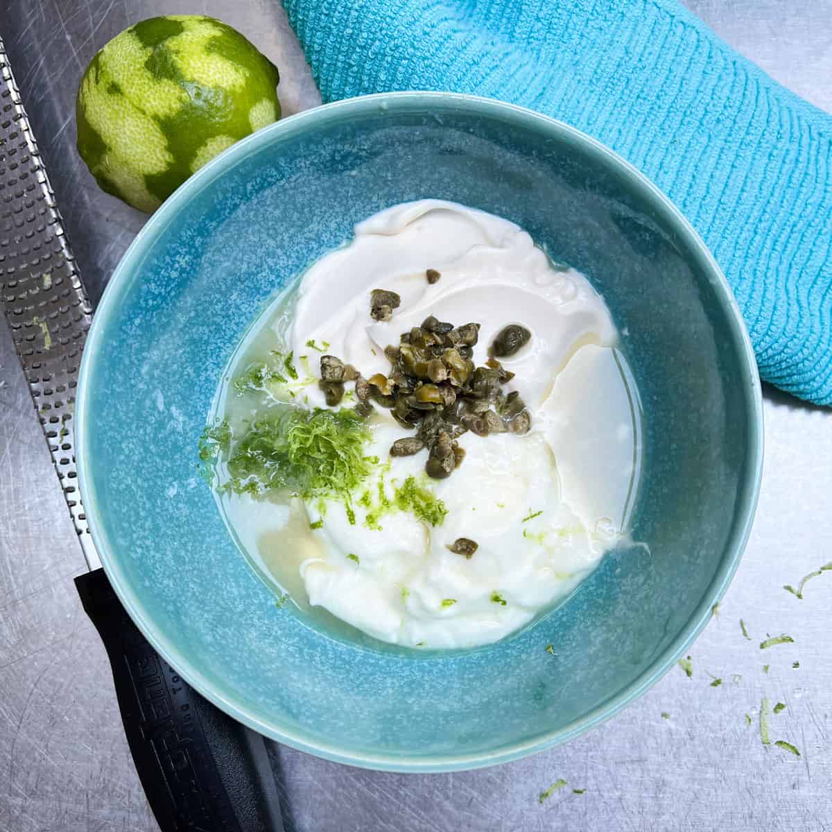 blue bowl filled with yogurt, mayo, lime juice, lime zest and chopped capers