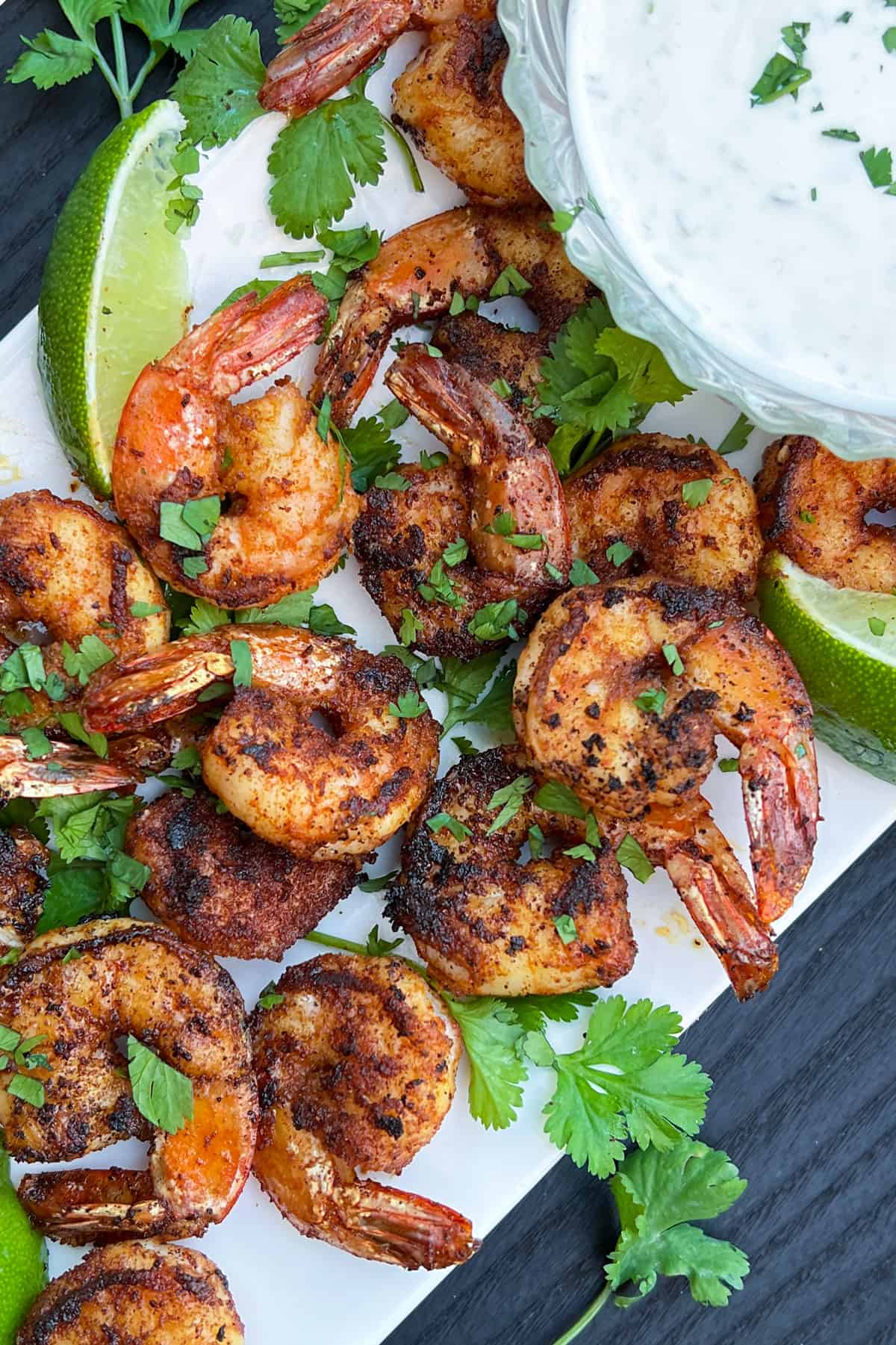 a dozen spice crusted sauteed shrip on a white platter topped with chopped cilantro