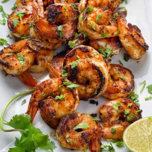 a dozen spice crusted sauteed shrimp on a white platter sprinkled with chopped cilantro