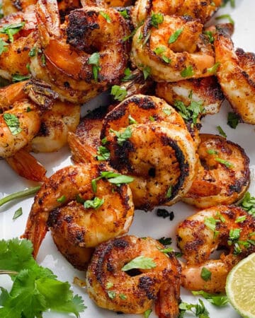 a dozen spice crusted sauteed shrimp on a white platter sprinkled with chopped cilantro