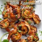 A dozen or so sautéed shrimp on a platter with a small bowl of remoulade sauce, half a lime and a sprig of parsley.