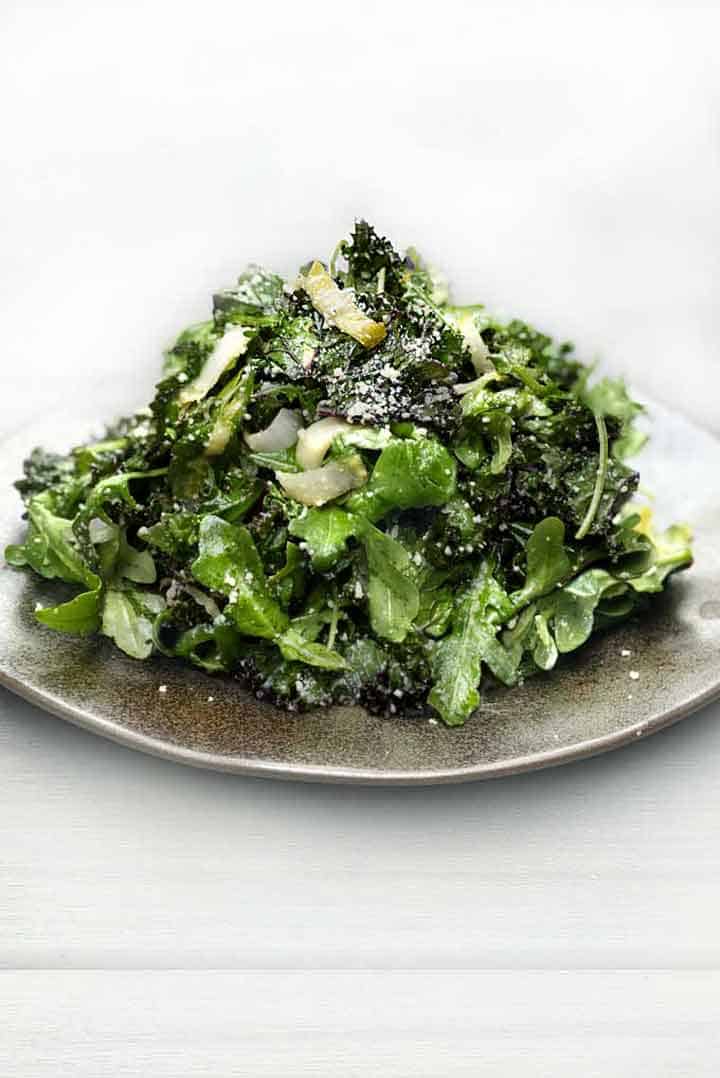 green salad stacked high on a light grey plate, a sprinkle of grated parmesan on top of the pile of salad greens.