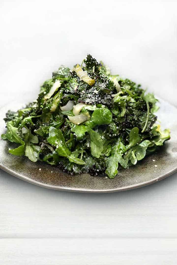 green salad stacked high on a light grey plate, a sprinkle of grated parmesan on top of the pile of salad greens.