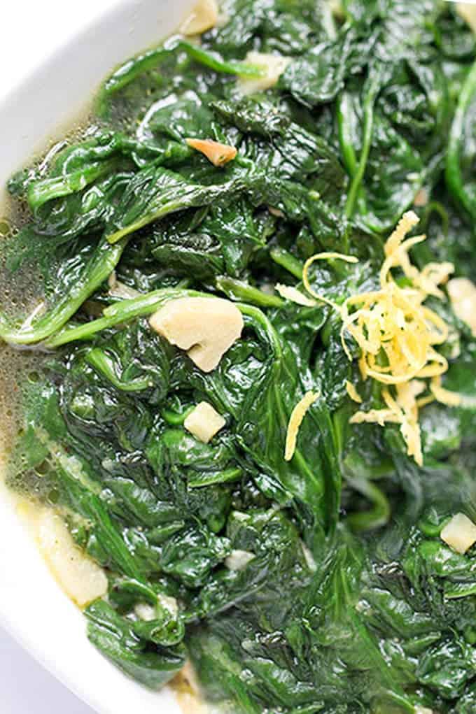close up of sauteed spinach with bits of garlic and grated lemon zest on top