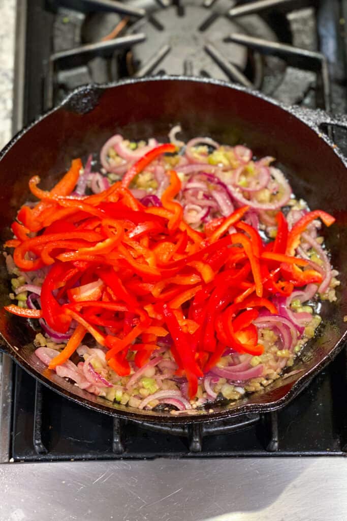 sliced red bell peppers added to a skillet with sautéd red onions and celery