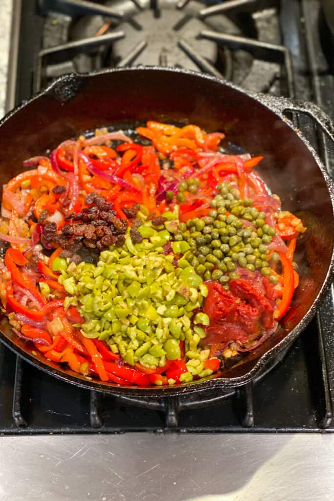 capers, chopped green olives, yellow raising and tomato paste added to a skillet with vegetables