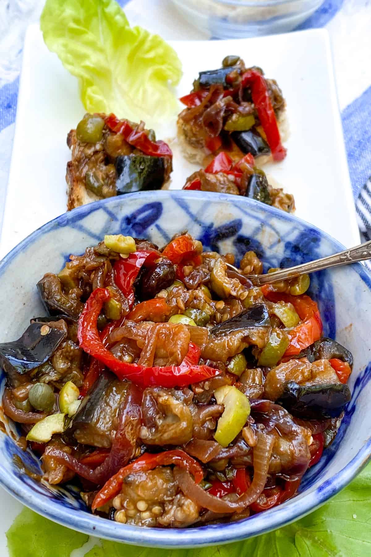 bowl of caponata showing stewed pieces of eggplant, sliced peppers, chopped olives and capers.