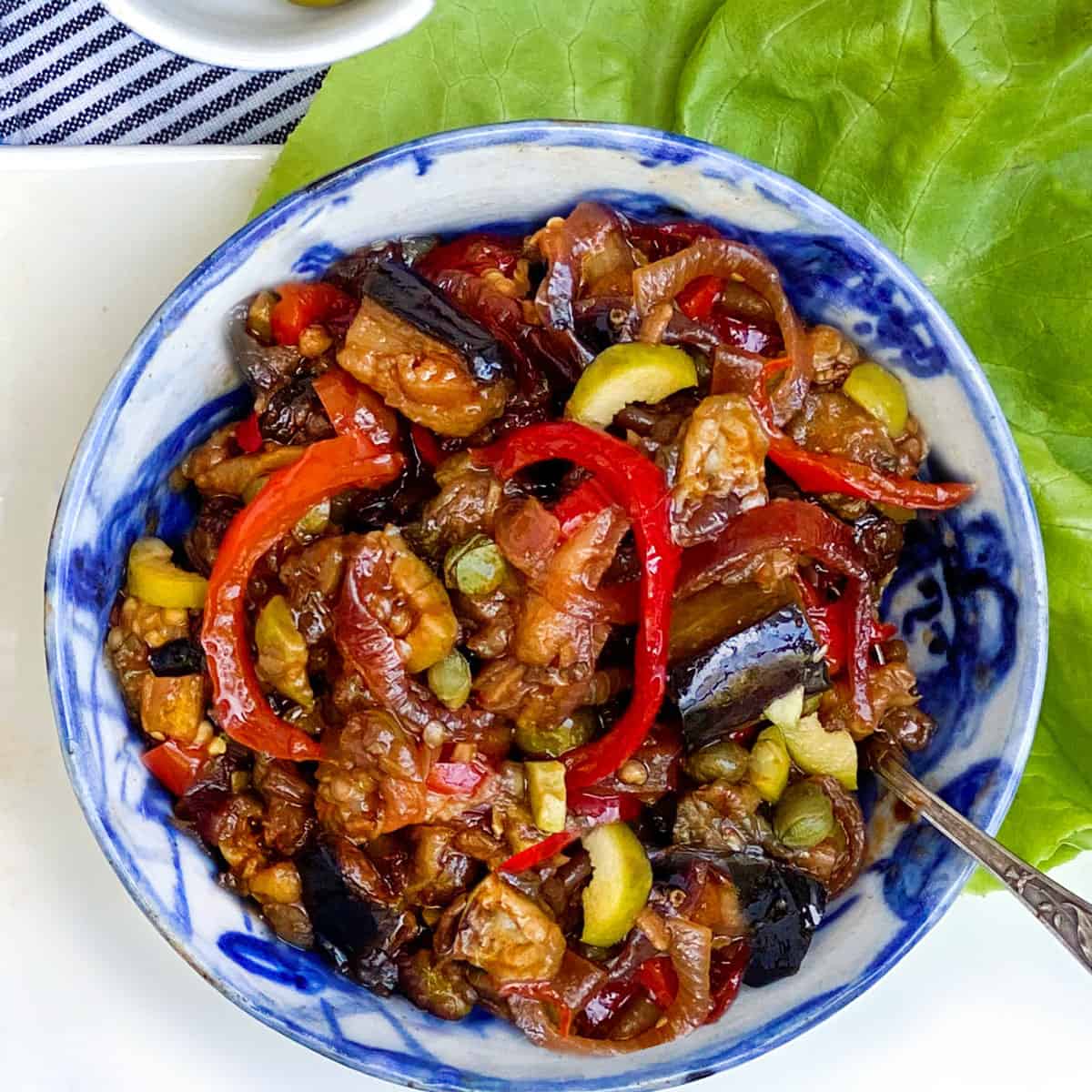 caponata - eggplant relish with bell peppers, olives, capers and onions - in a ceramic bowl with a silver spoon