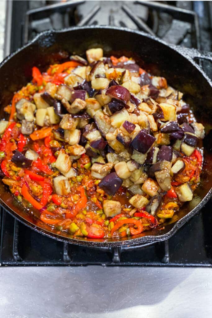 cubes of sautéd eggplant added to a skillet with other sautéd vegetables, olives and capers