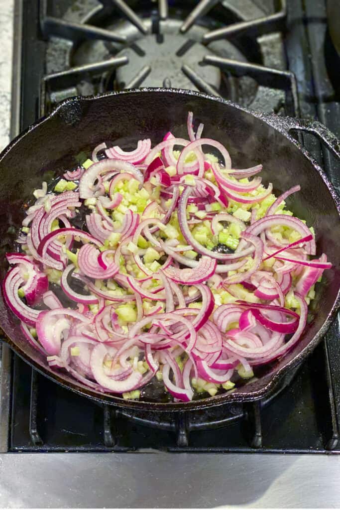 red onions and chopped celery sautéing in a cast iron skillet
