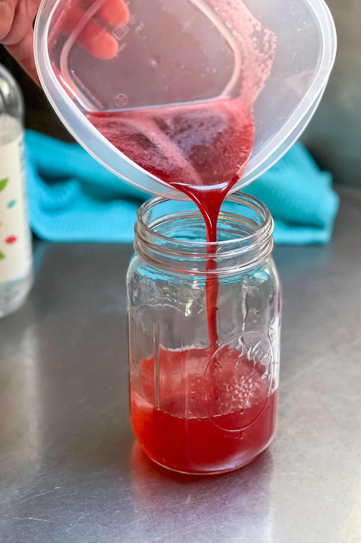 Berry shrub syrup being poured from a plastic container into a mason jar