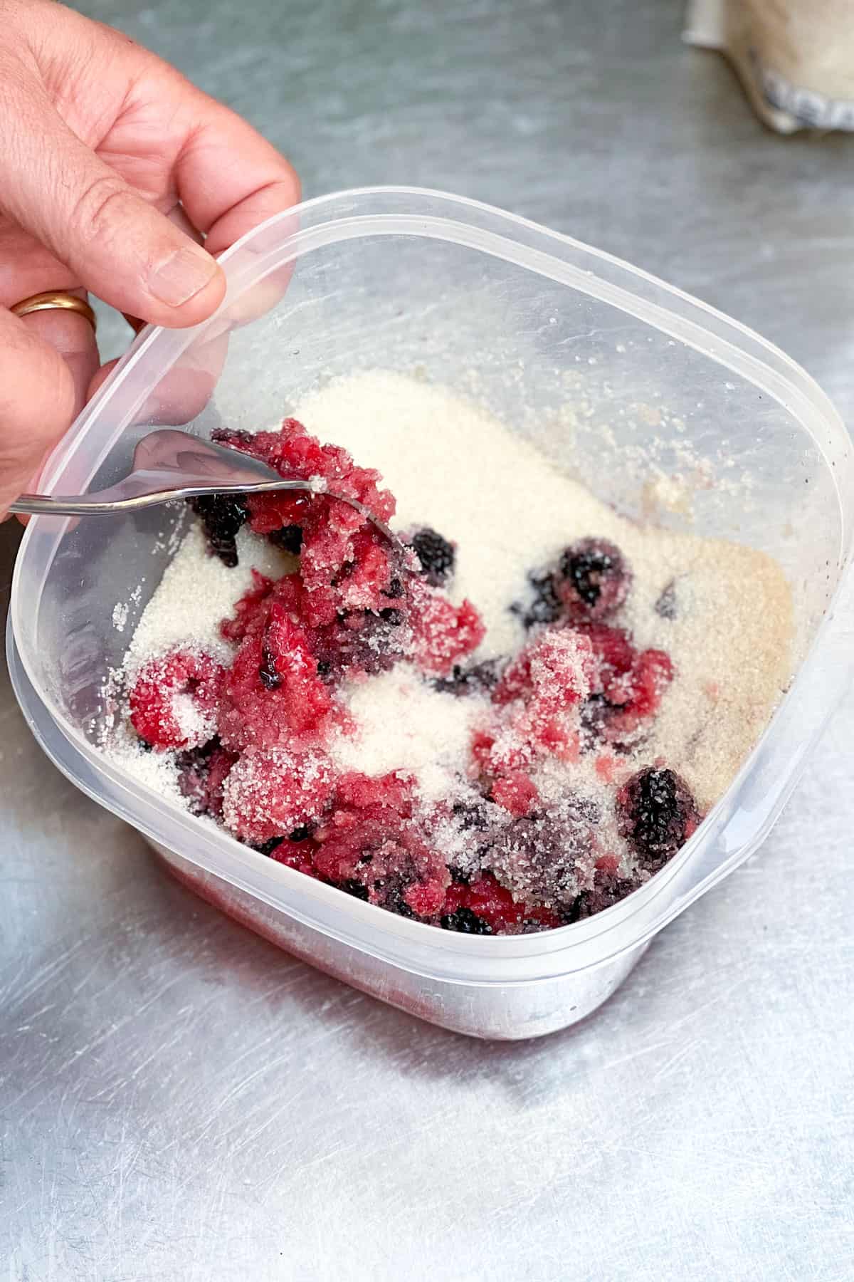 bruised raspberries and blackberries mixed with sugar in a plastic container