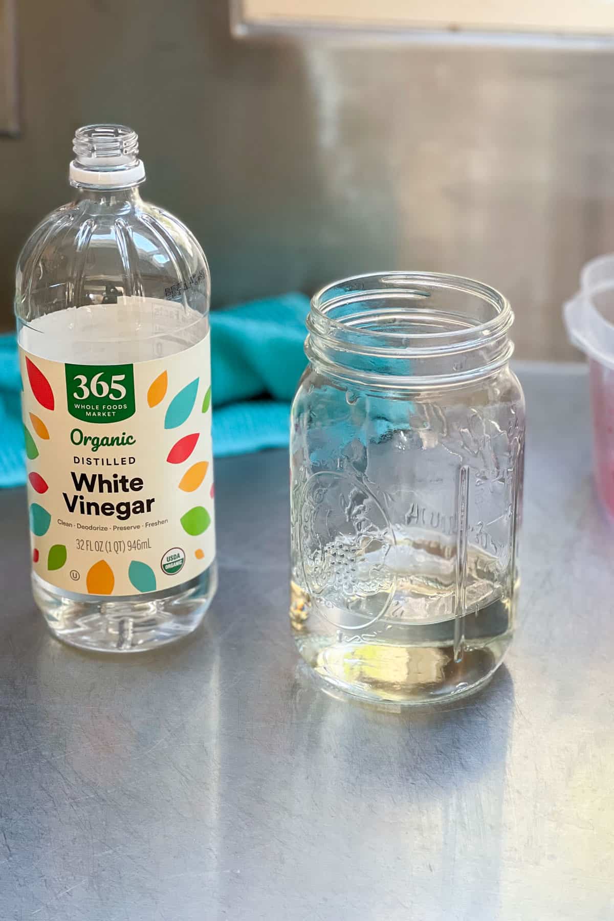 a bottle of white vinegar next to a glass mason jar one quarter filled with white vinegar