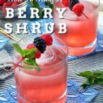 Berry shrub drink in a glass tumbler with a garnish on top of a toothpick with three berries and a mint sprig.