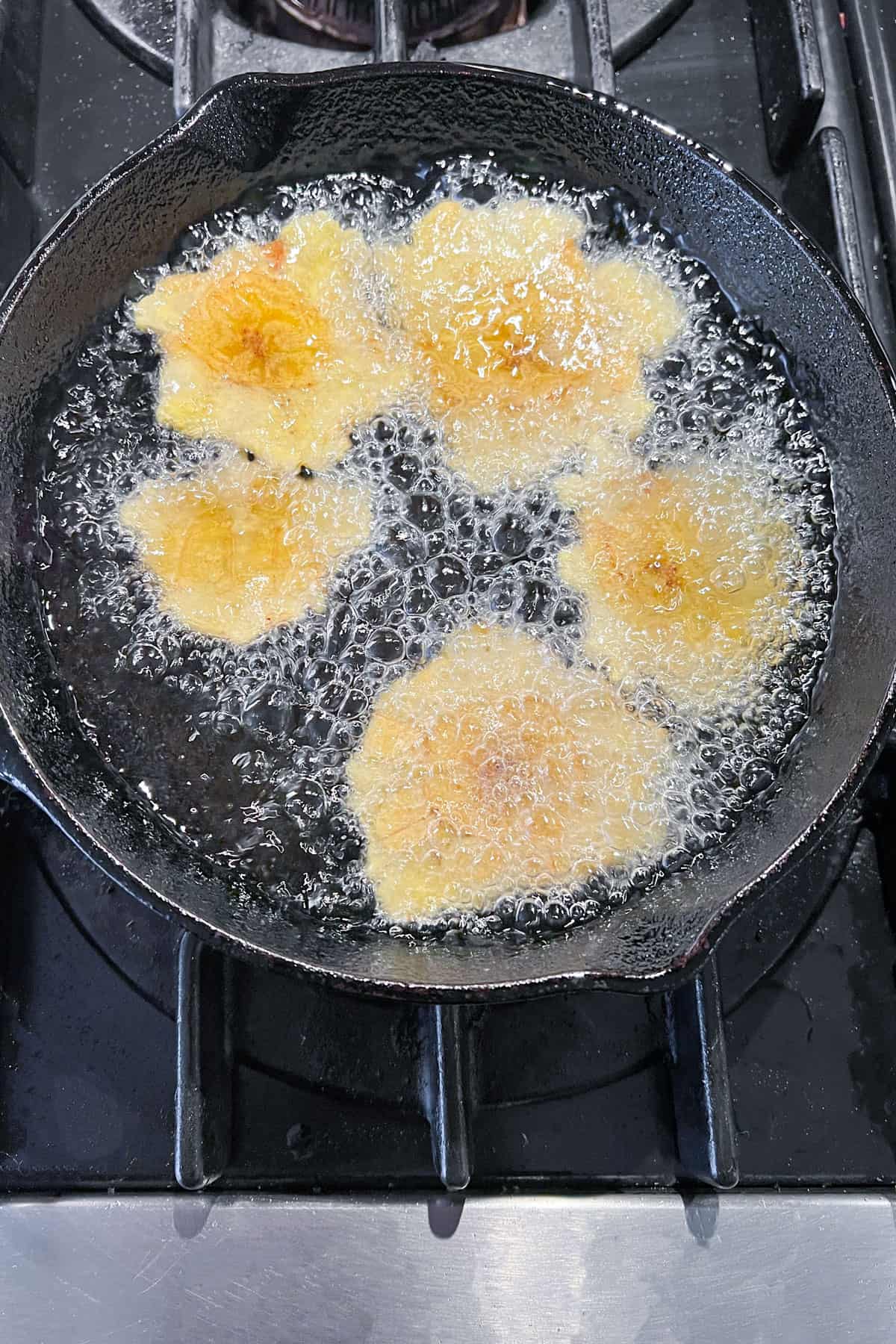 5 patacones frying in a small cast iron skillet