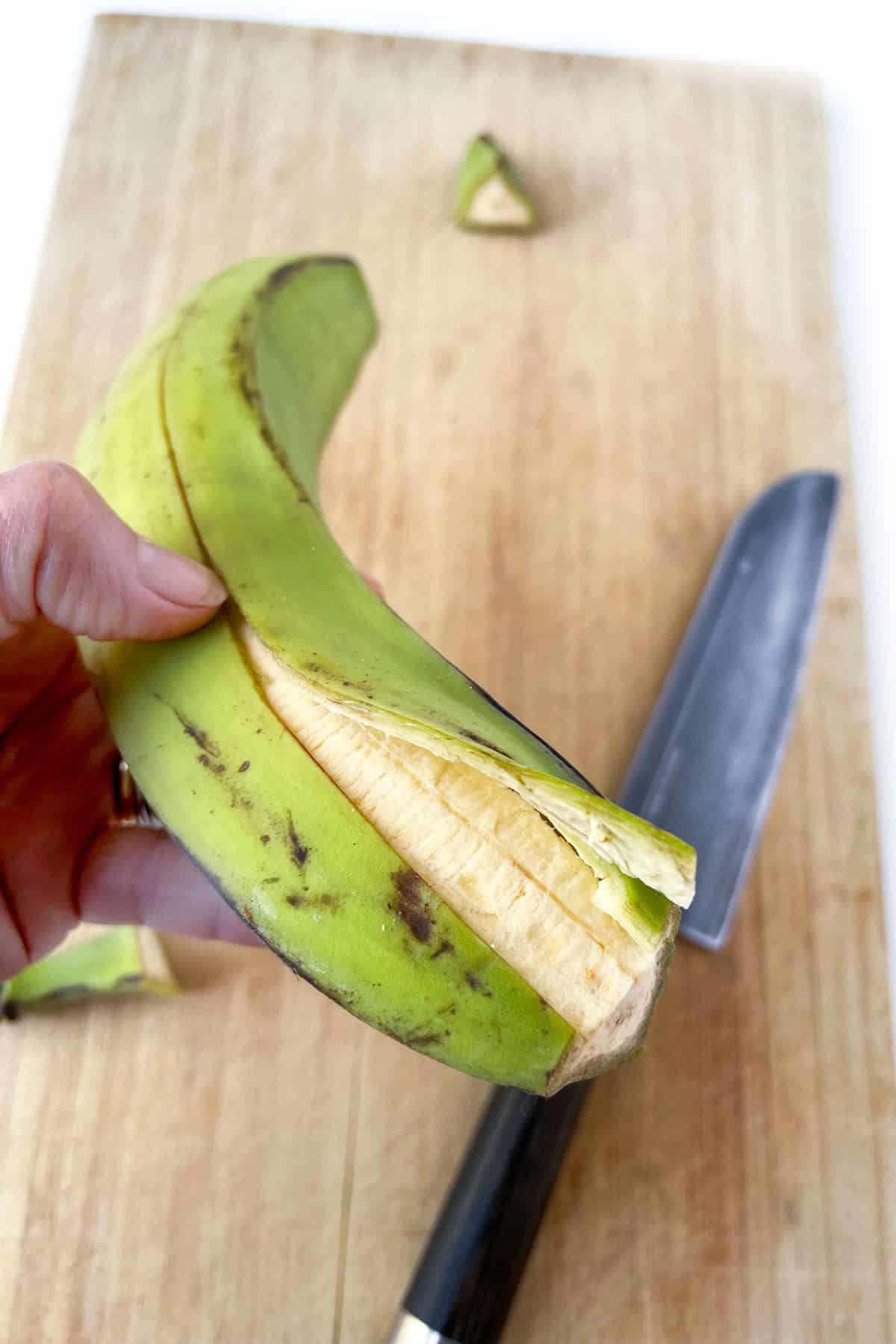 a green plantain with the skin partially peeled off and the flesh showing beneath