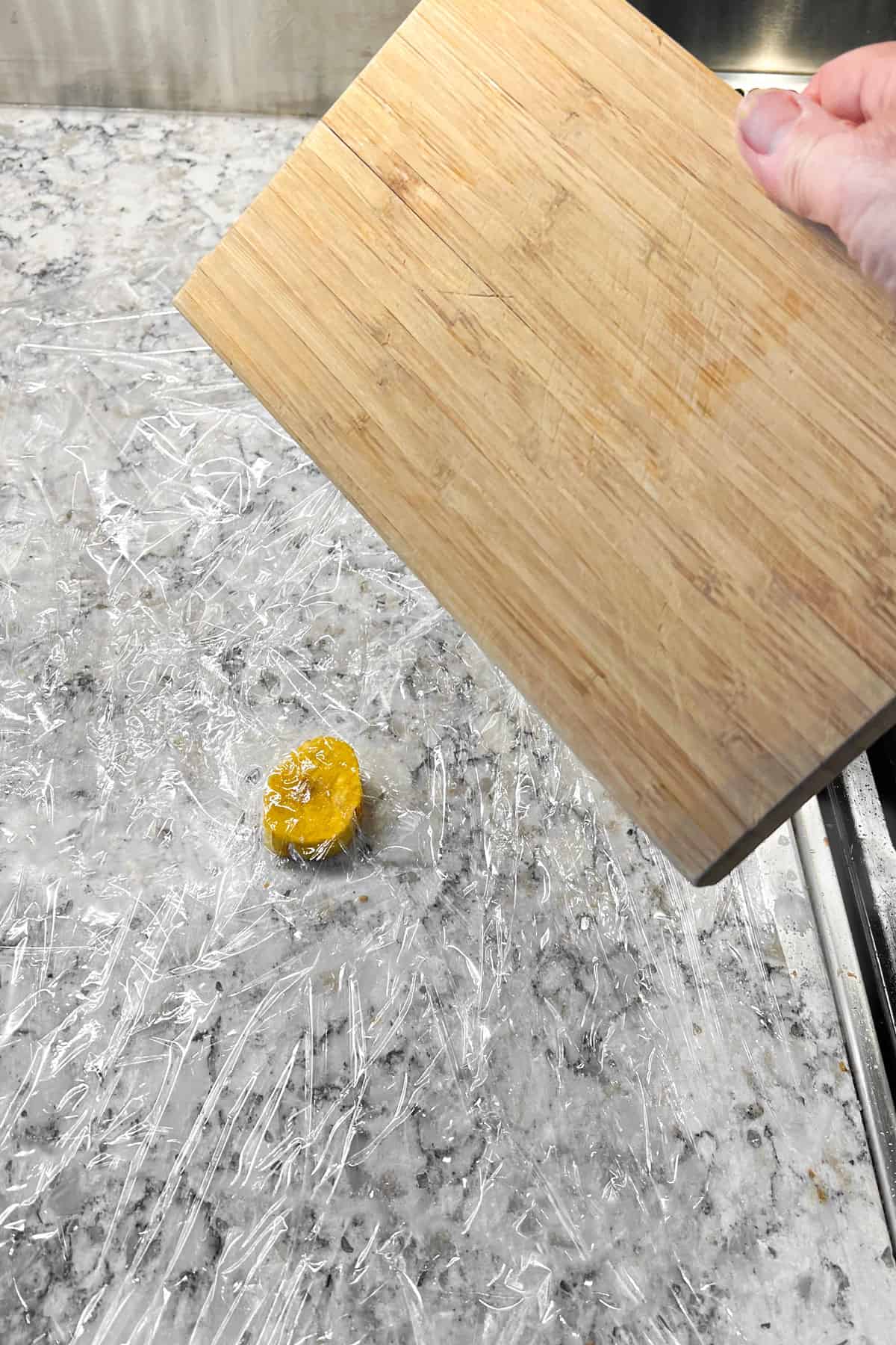 a small wooden cutting board hovering over a small slice of green plantain that's sitting on a countertop