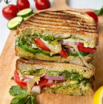 cheese panini grilled Mumbai sandwich on wooden cutting board with 3 cherry tomatoes in the background