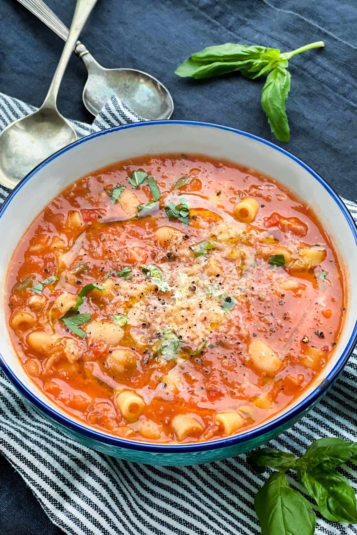 A porcelain bowl filled with pasta e fagioli soup with tiny tubes of pasta and cannellini beans, topped with finely grated parmesan cheese and chopped basil.