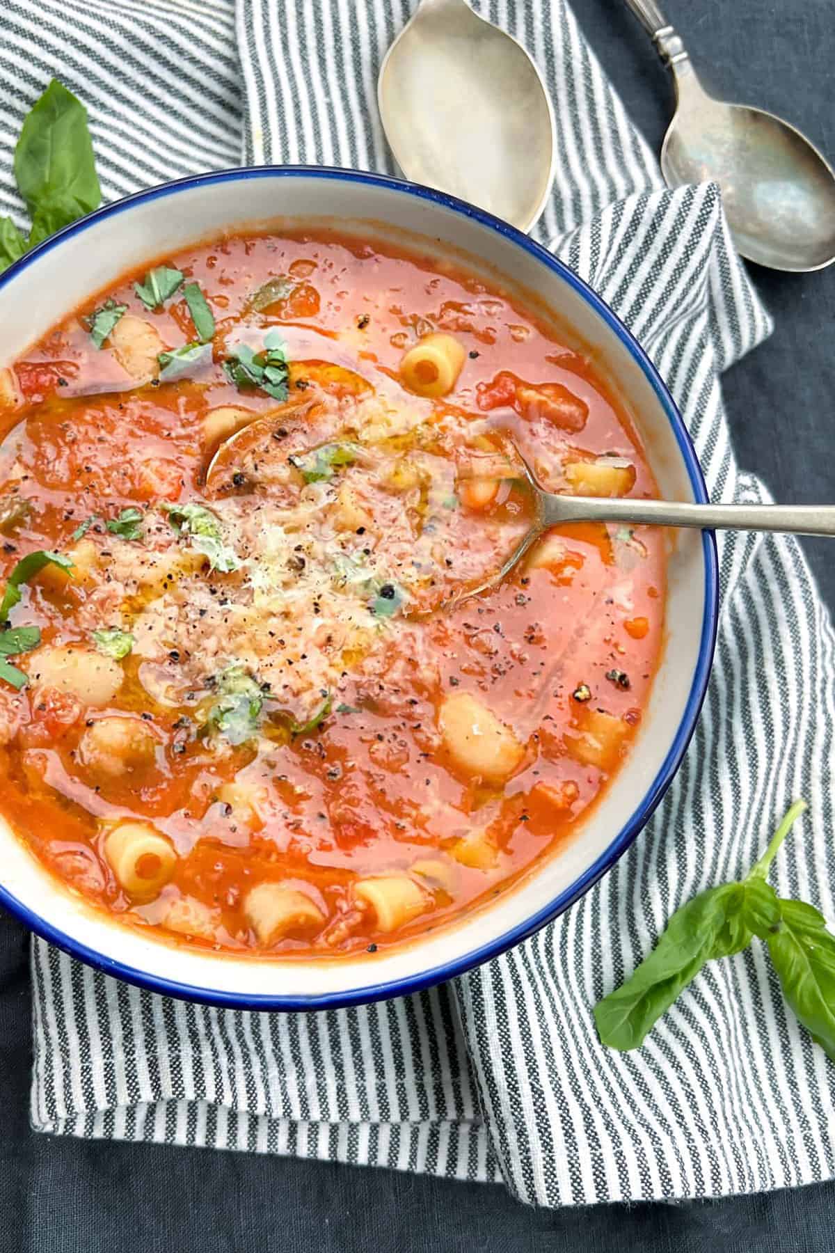 A porcelain bowl filled with pasta e fagioli soup with tiny tubes of pasta and cannellini beans, topped with finely grated parmesan cheese and chopped basil.