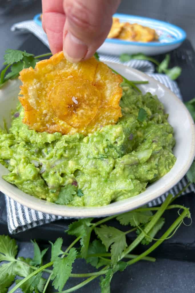 one patacone chip being dipped into a bowl of guacamole