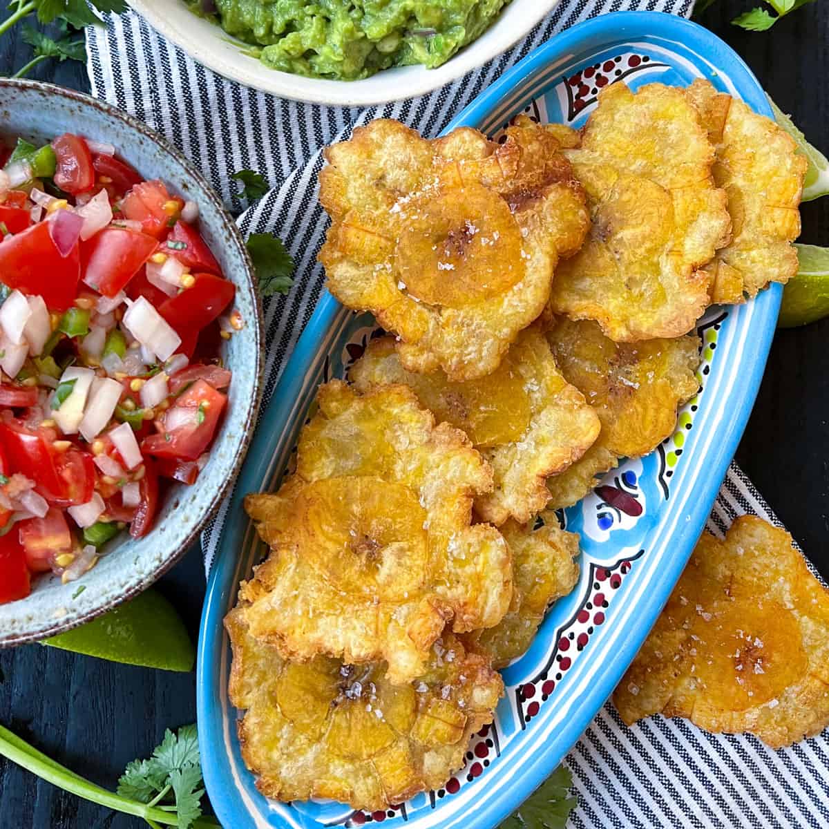 oval serving dish filled with patacones, plantain chips, with a bowl of guacamole and a bowl of pico de gallo by the side