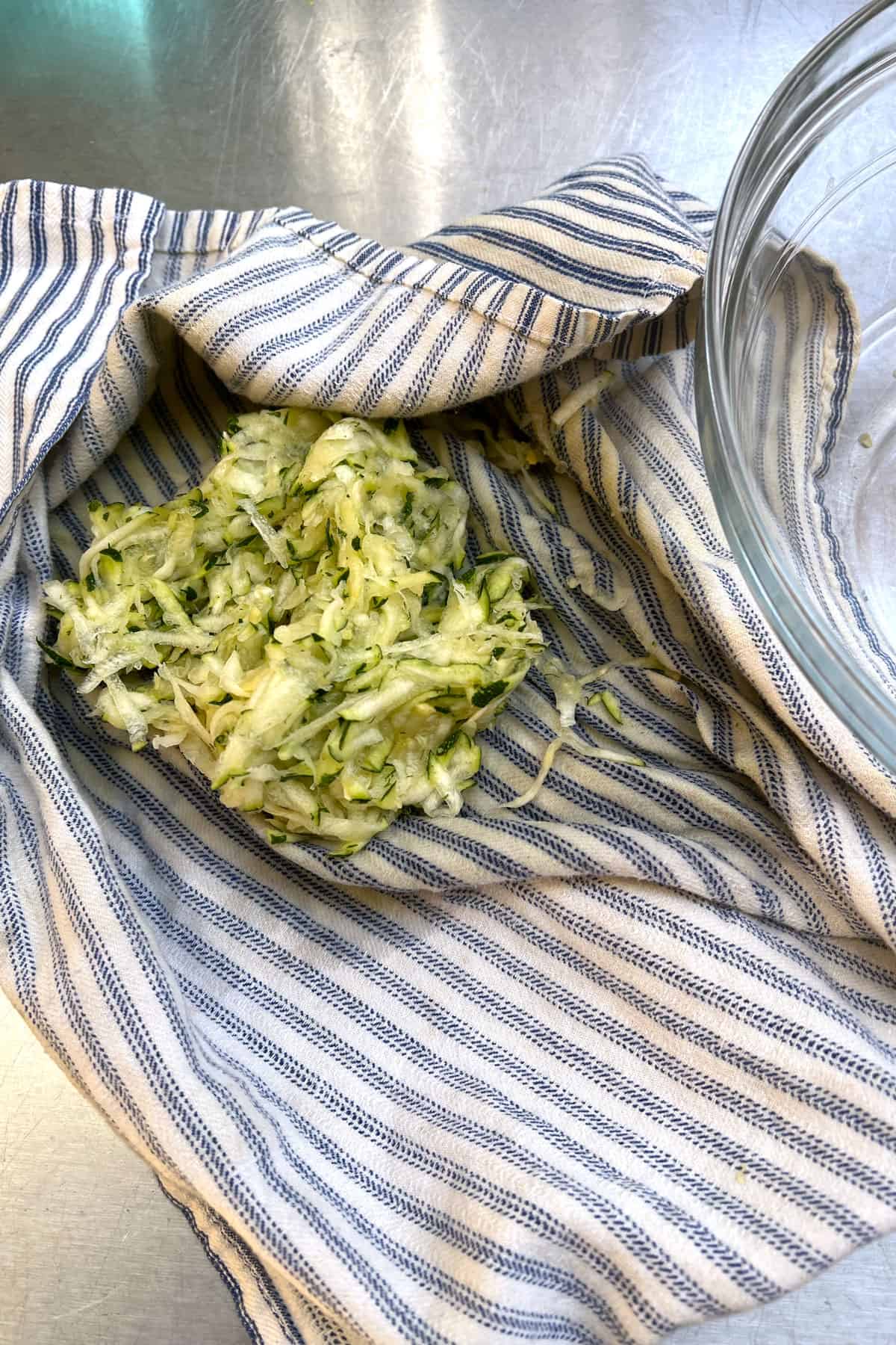 Shredded salted zucchini and summer squash in a striped dish towel
