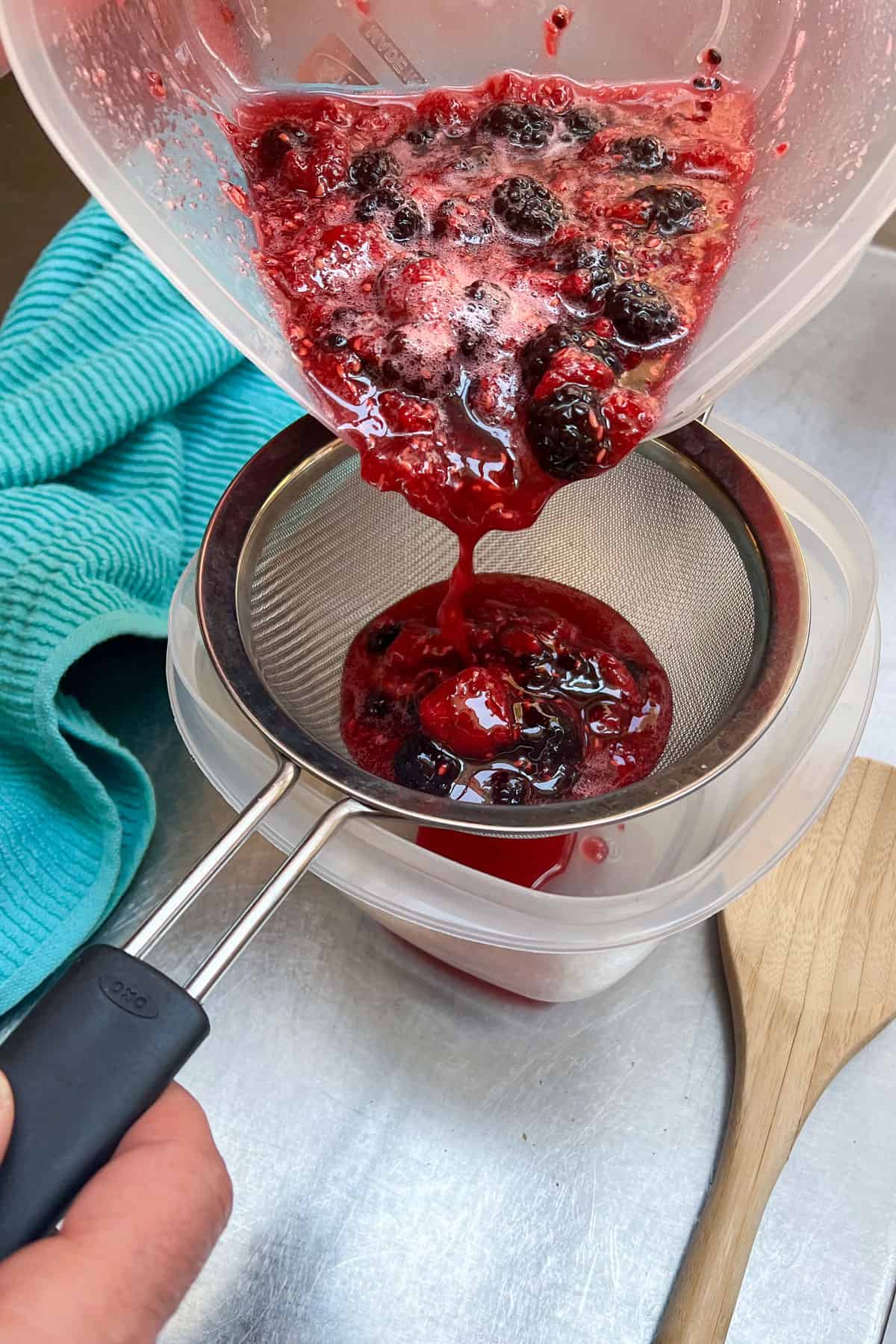 macerated berries with their juices being poured through a small mesh stainer into a plastic container below