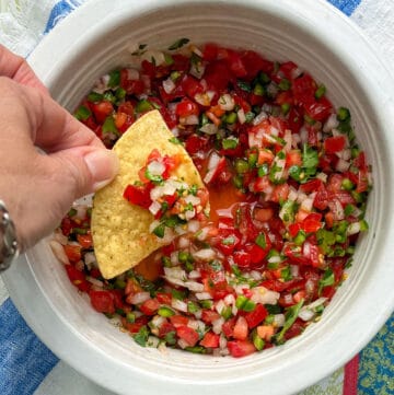 A corn tortilla chip being dipped into a bowl filled with finely chopped salsa fresca made from tomatoes, chilies, onion and cilantro.