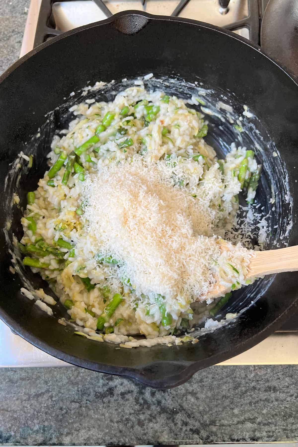 Finely grated parmesan cheese being stirred through a pot of asparagus risotto