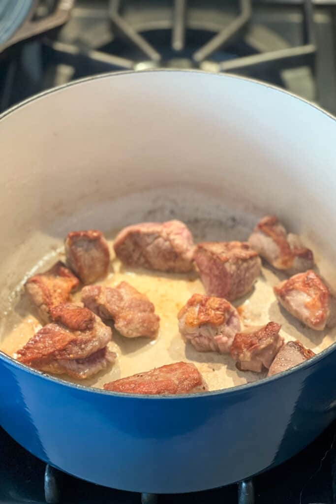 about a dozen chunks of lamb stew meat browning in a Dutch oven.