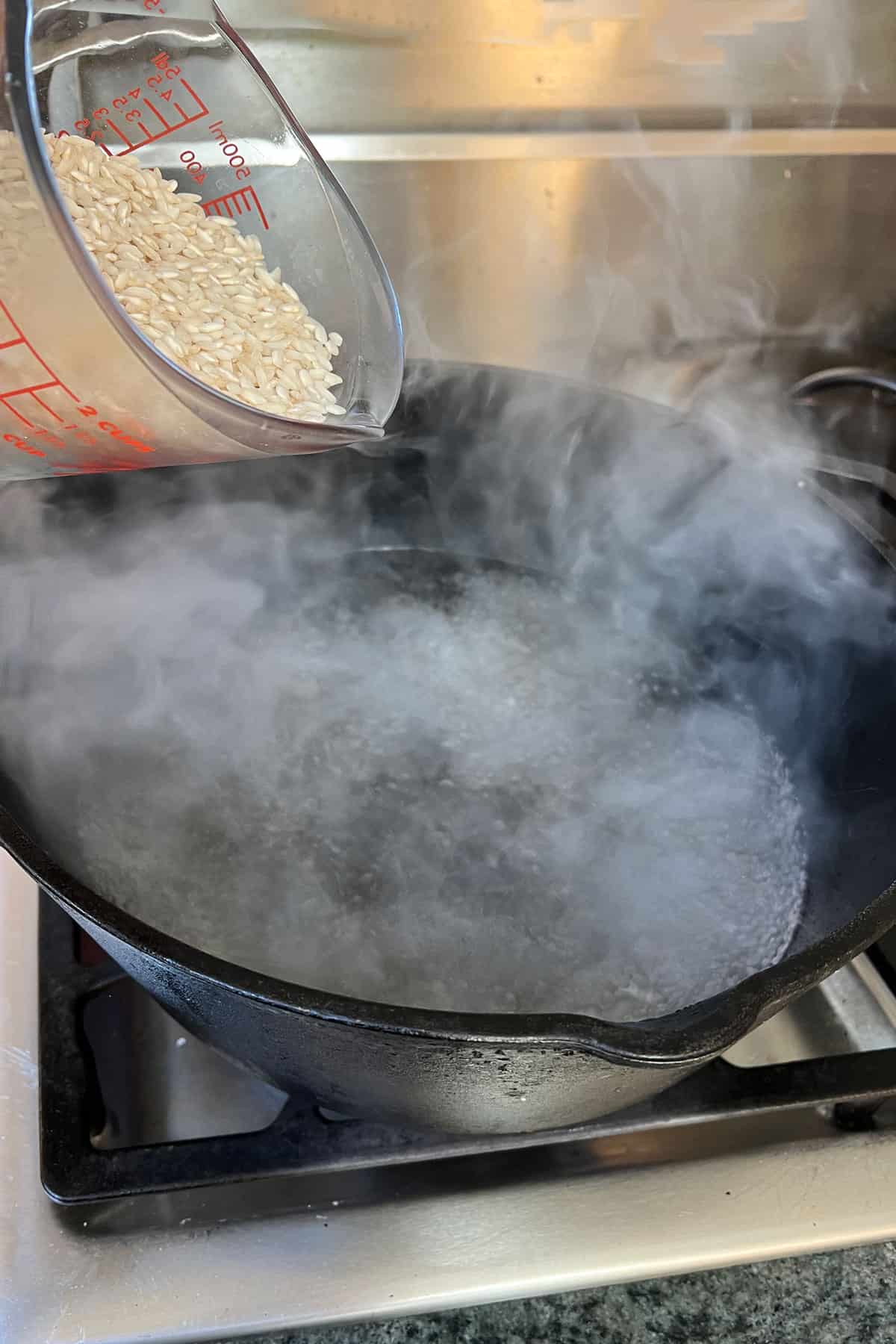 short grain rice being poured from a measuring cup into a pot of boiling water