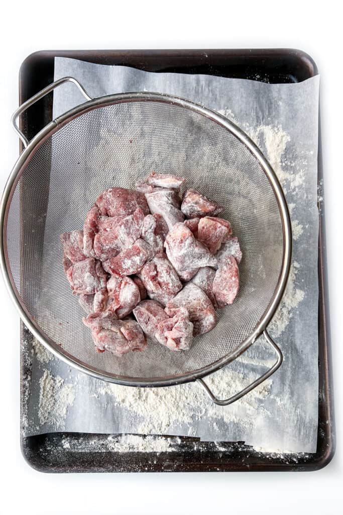 Floured chunks of lamb in a mesh colander
