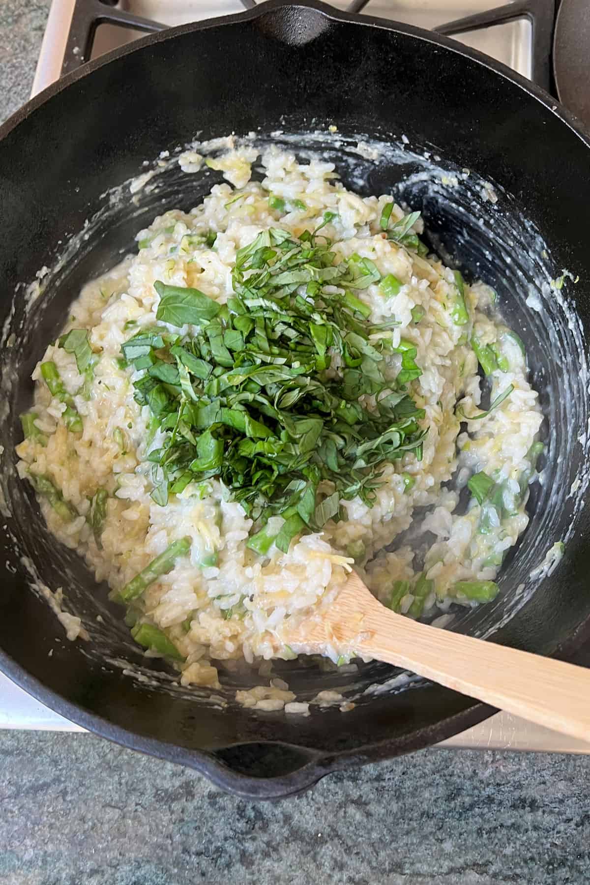 Fresh slivered basil being stirred through a pot of lemon asparagus risotto