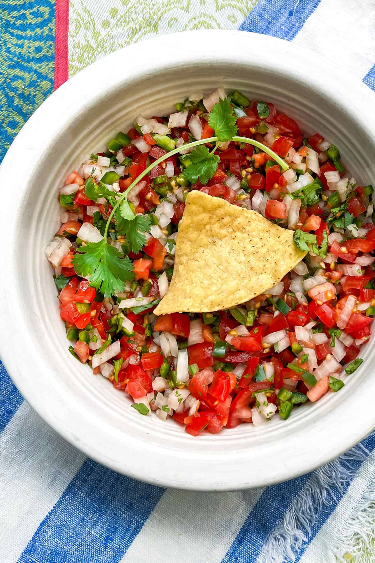 Salsa fresca in a serving bowl with a corn tortilla chip in the center.