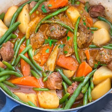 Pot of lamb stew with chunks of lamb, carrots, potatoes and green beans.