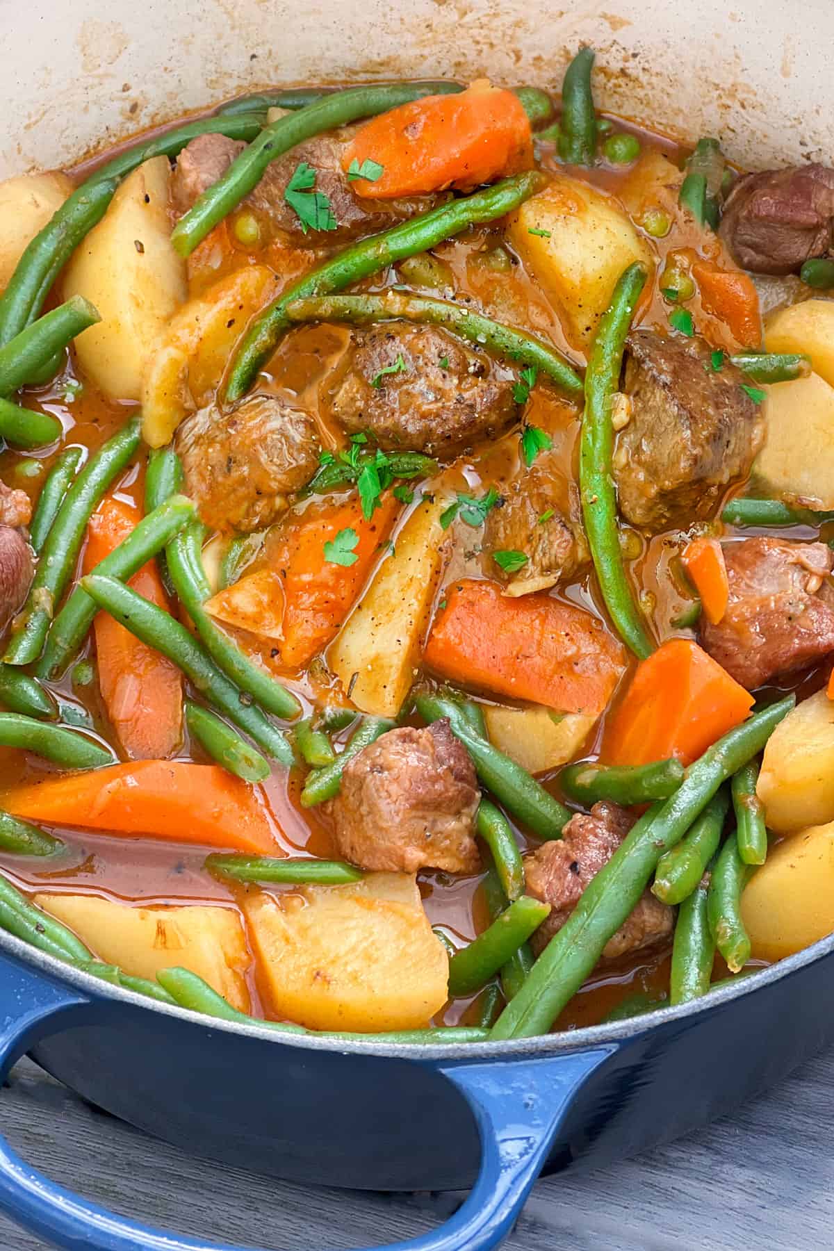 Dutch oven filled with lamb stew that has carrots, potatoes, peas and green beans