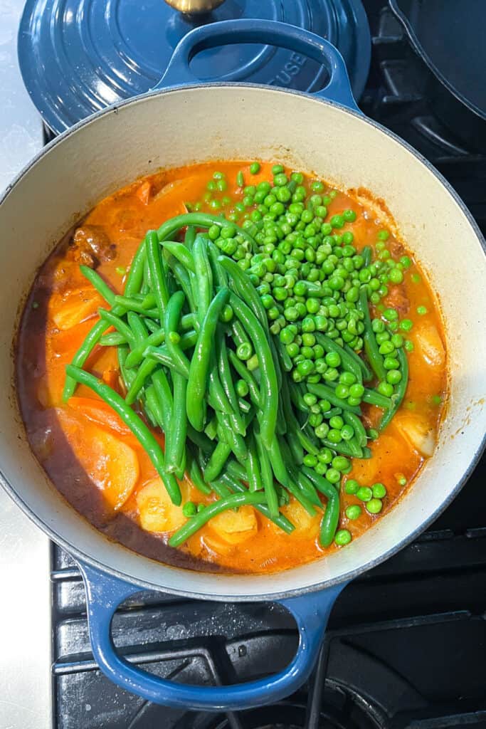 blanched green beans and sweet pees added to a Dutch oven filled with lamb stew.
