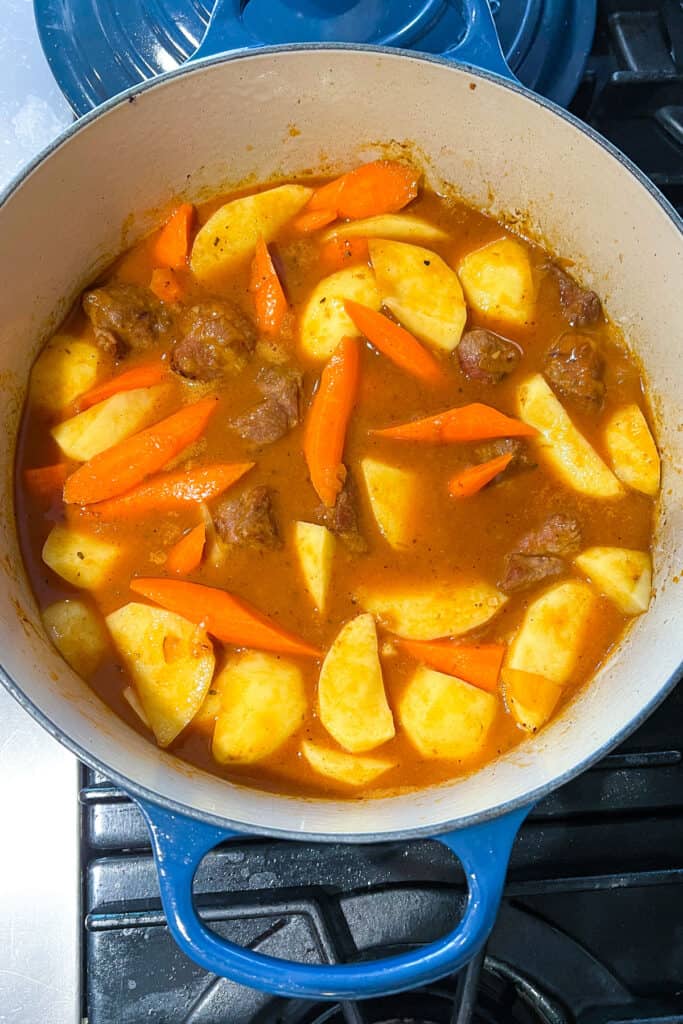 raw chunks of potatoes and carrots added to a Dutch oven with lamb and broth.