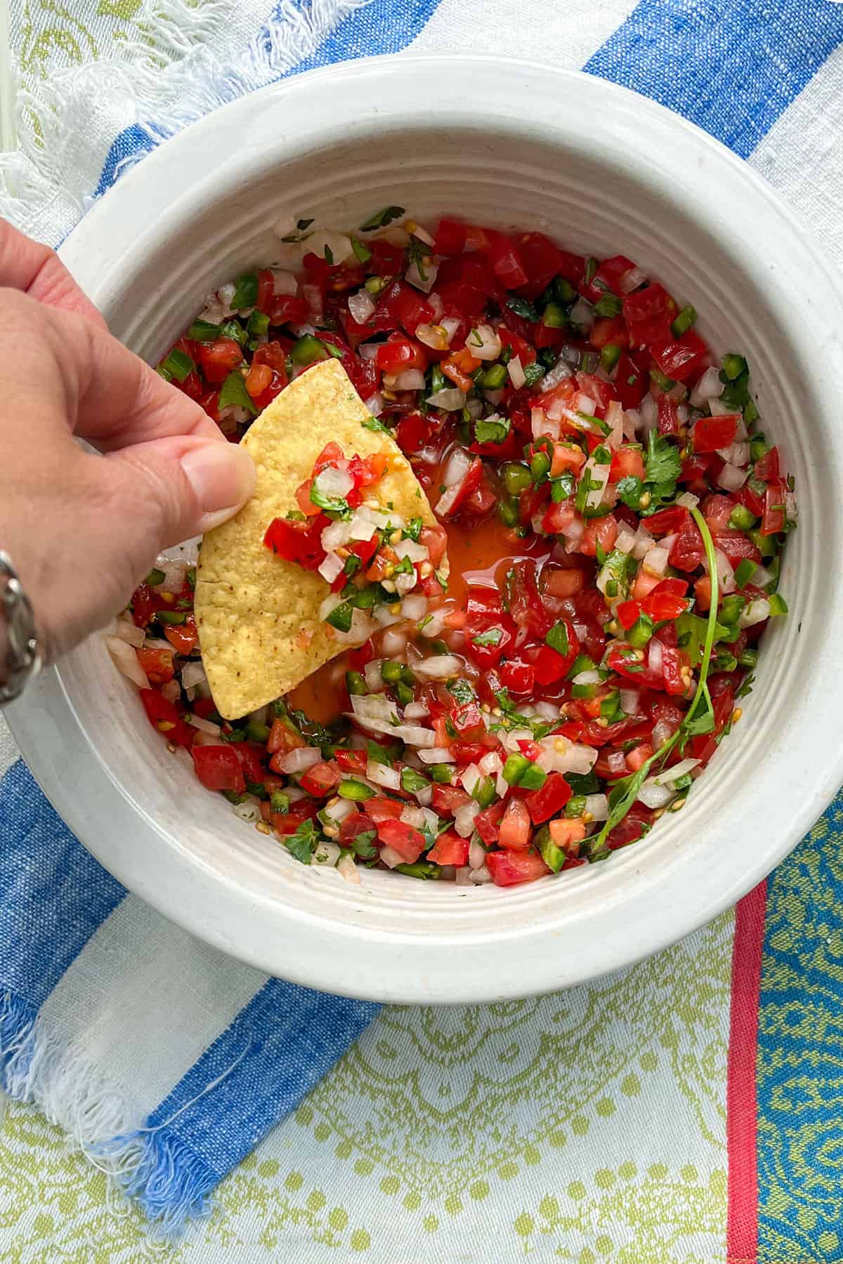 A corn tortilla chip being dipped into a bowl filled with finely chopped salsa fresca made from tomatoes, chilies, onion and cilantro.