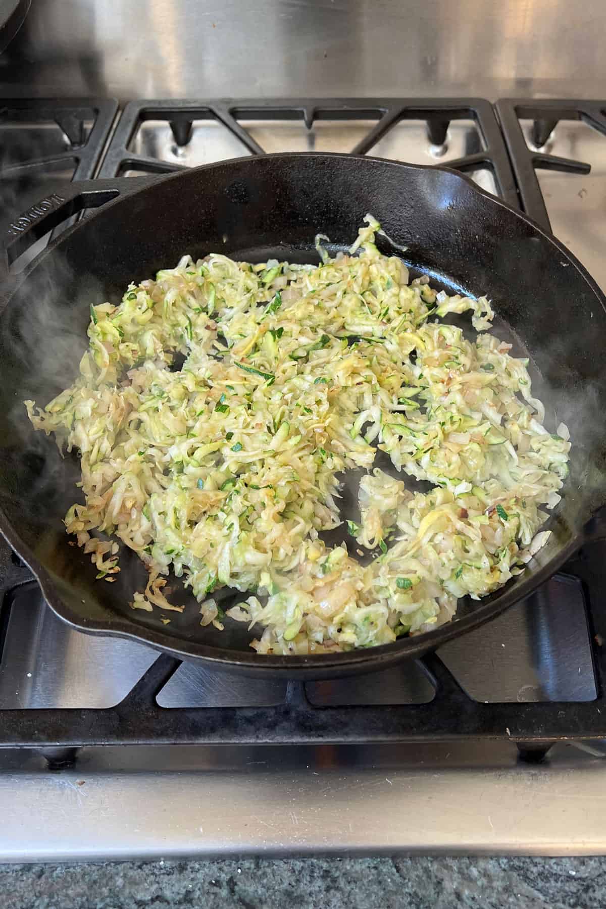 Shredded zucchini and summer squash cooking in a cast iron skillet