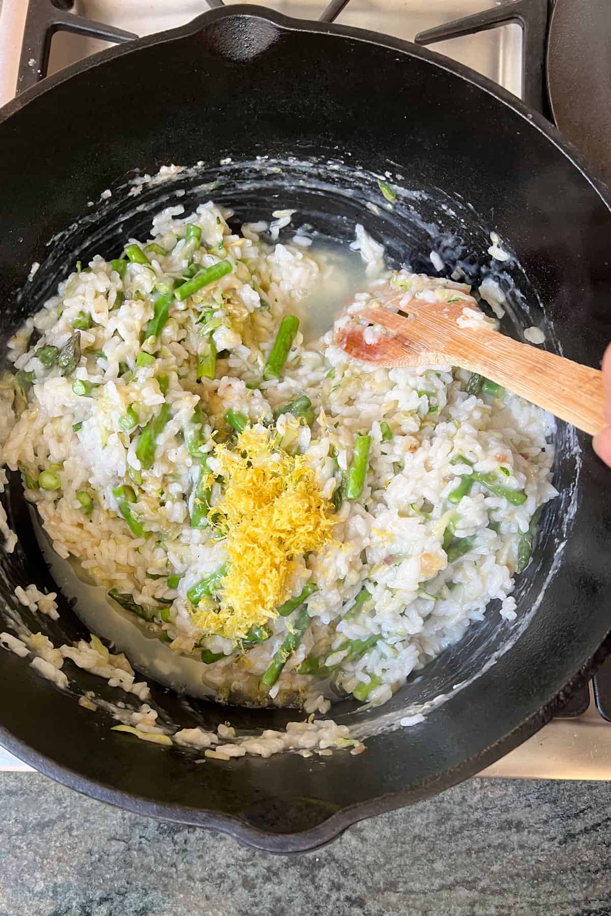 lemon zest and juice being stirred through risotto in a Dutch oven