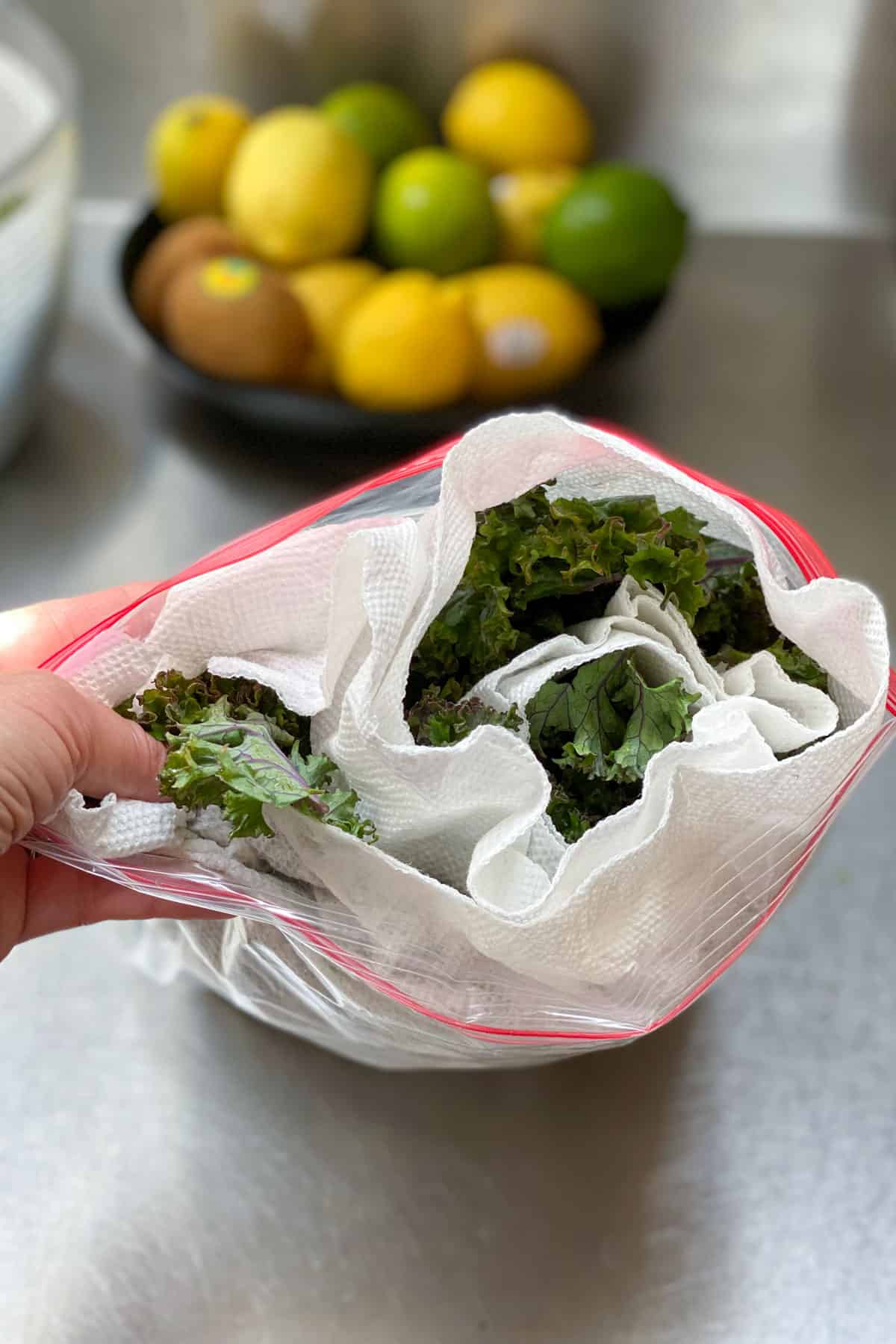 a roll of kale leaves inside a plastic ziplock bag with a bowl of lemons and limes in the background