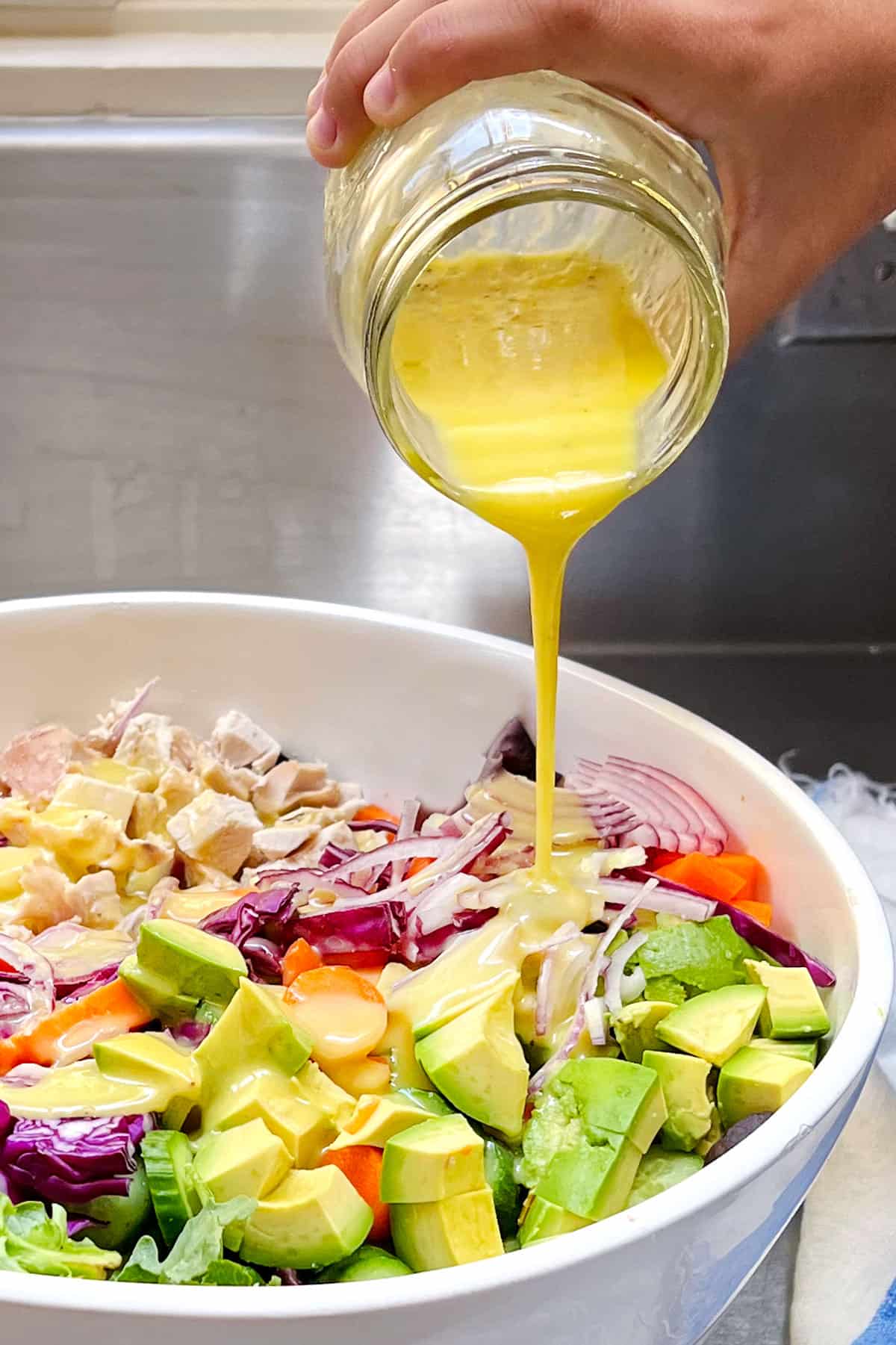 lemon vinaigrette being poured in a stream from a mason jar into a bowl of colorful salad