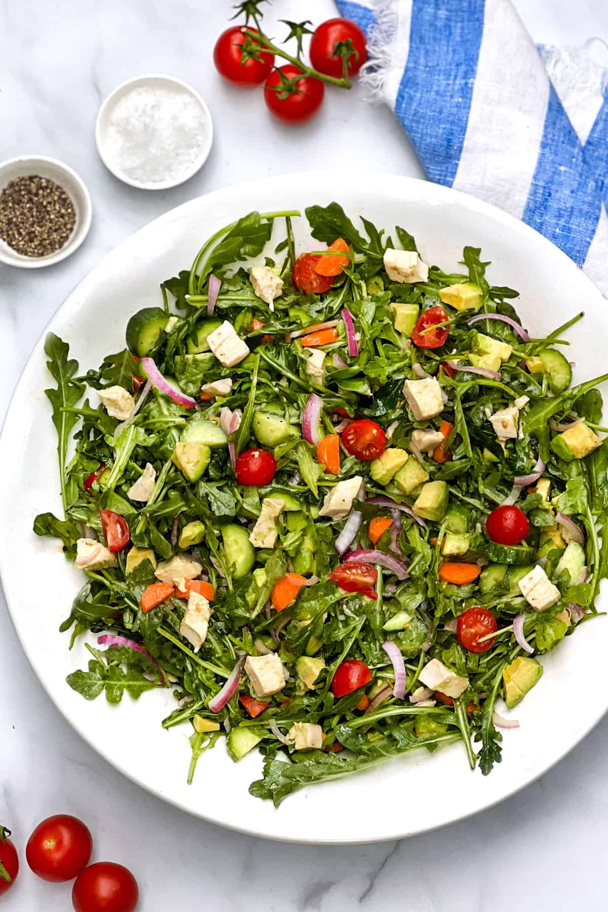 serving bowl filled with colorful chopped salad of arugula, cherry tomatoes, chicken, cucumbers, carrots and red onons